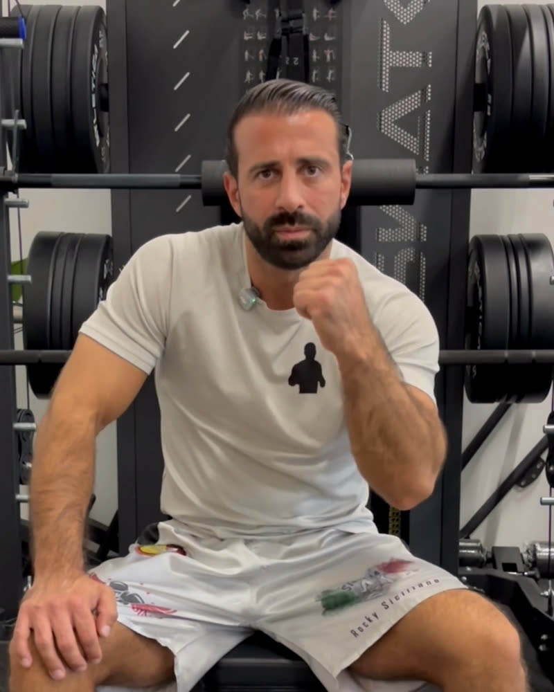 Rocky Siciliano mit geballter Faust vor einem Hantelrack
